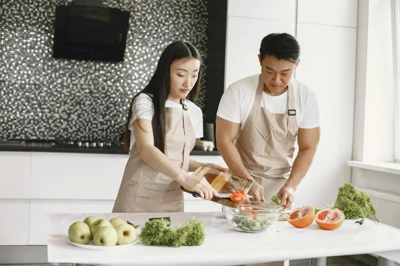 Asian couple making a healthy salad together at home in a modern kitchen setting.